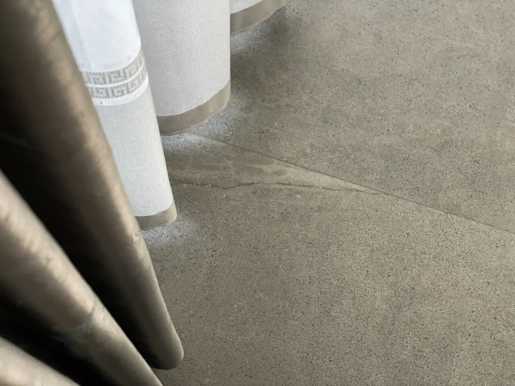 Microcementgolv med naturlig struktur i dämpad färg, delvis täckt av ljusa textilgardiner.